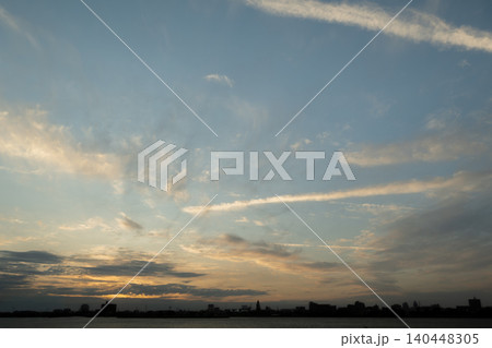 広大な夕焼け空と飛行機雲が掛かる水辺の街並みのシルエット 広大な夕焼け空と飛行機雲が掛かる水辺の街並みのシルエット 140448305