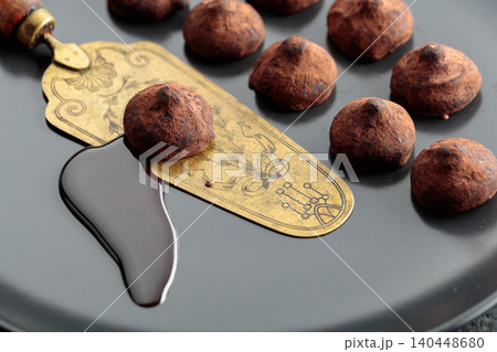 Chocolate truffles, chocolate sauce, and vintage brass cake server on a black plate. Chocolate truffles, chocolate sauce, and vintage brass cake server on a black plate. 140448680