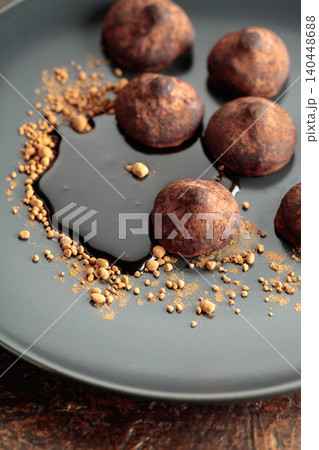 Chocolate truffles with cocoa powder and chocolate sauce on a black plate. Chocolate truffles with cocoa powder and chocolate sauce on a black plate. 140448688