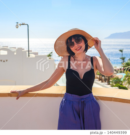 A woman at a resort holds her hat on her head against the strong wind A woman at a resort holds her hat on her head against the strong wind 140449399