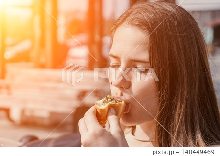 Woman eating pastry outdoors while enjoying a snack during a sunny day in the city with warm golden light Woman eating pastry outdoors while enjoying a snack during a sunny day in the city with warm golden light 140449469