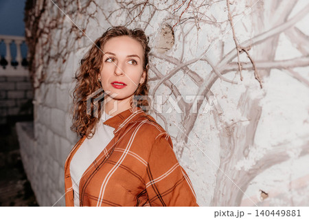 Woman portrait hair leaning against a rustic white wall wearing an orange plaid shirt in soft evening light 140449881