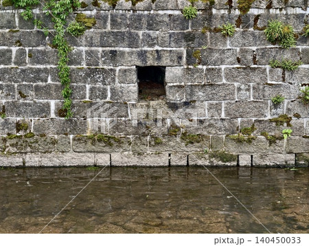 Mossy stone riverside wall with small drainage opening Mossy stone riverside wall with small drainage opening 140450033