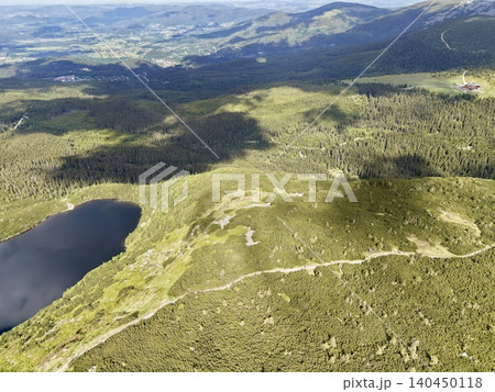 Aerial view of mountain ridge, forest and alpine lake under scattered clouds Aerial view of mountain ridge, forest and alpine lake under scattered clouds 140450118