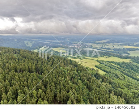 Aerial view of dense evergreen forest and patchwork farmland under dramatic cloudy sky Aerial view of dense evergreen forest and patchwork farmland under dramatic cloudy sky 140450302