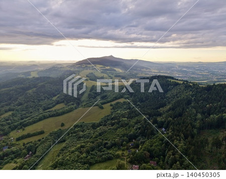 Rolling green hills and forested valley under dramatic cloudy sky at sunset Rolling green hills and forested valley under dramatic cloudy sky at sunset 140450305