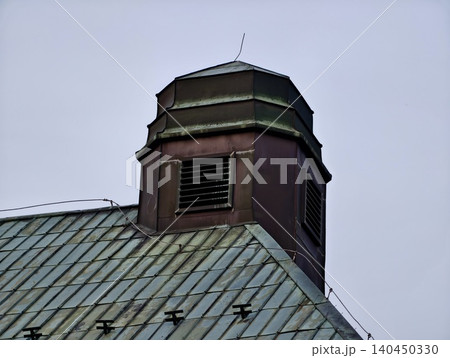 Aged metal roof with ventilated rooftop cupola under overcast sky 140450330