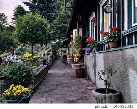 Garden pathway beside a cottage with potted flowers and greenery 140450332