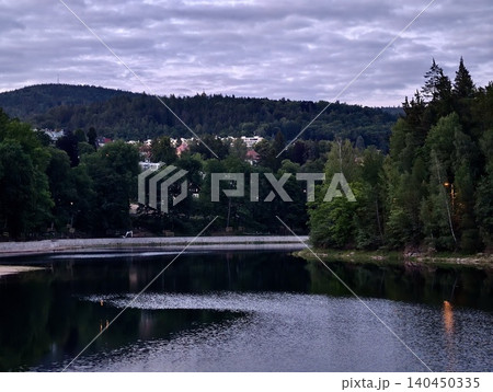 Calm lake with forested shoreline and hillside homes under cloudy sky Calm lake with forested shoreline and hillside homes under cloudy sky 140450335