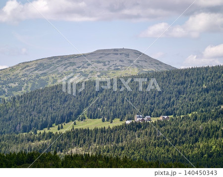 Mountain lodge nestled in dense evergreen forest beneath rounded summit Mountain lodge nestled in dense evergreen forest beneath rounded summit 140450343