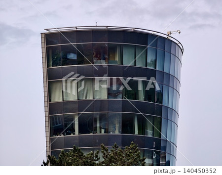 Curved glass office tower with reflective windows and rooftop railing Curved glass office tower with reflective windows and rooftop railing 140450352
