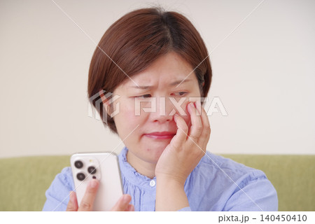 スマホを見て不安そうに考え込む女性 スマホを見て不安そうに考え込む女性 140450410