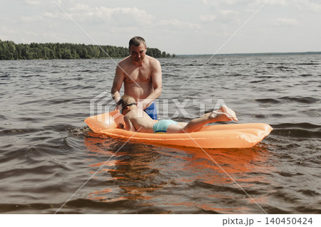 father son enjoying relaxing summer day, floating inflatable mattress calm river. man holding child securely ensuring safety while both enjoy water. Outdoor recreation, family vacation, summer nature father son enjoying relaxing summer day, floating inflatable mattress calm river. man holding child securely ensuring safety while both enjoy water. Outdoor recreation, family vacation, summer nature 140450424