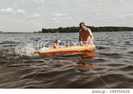father son enjoying relaxing summer day, floating inflatable mattress calm river. man holding child securely ensuring safety while both enjoy water. Outdoor recreation, family vacation, summer nature father son enjoying relaxing summer day, floating inflatable mattress calm river. man holding child securely ensuring safety while both enjoy water. Outdoor recreation, family vacation, summer nature 140450426