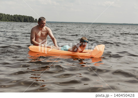 father son enjoying relaxing summer day, floating inflatable mattress calm river. man holding child securely ensuring safety while both enjoy water. Outdoor recreation, family vacation, summer nature father son enjoying relaxing summer day, floating inflatable mattress calm river. man holding child securely ensuring safety while both enjoy water. Outdoor recreation, family vacation, summer nature 140450428