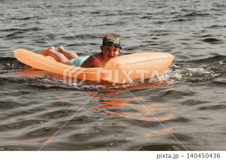 little boy joyfully plays orange inflatable mattress river, creating bright splashes around him. image conveys carefree joy and energy childhood summer day. water activities childre, family vacations little boy joyfully plays orange inflatable mattress river, creating bright splashes around him. image conveys carefree joy and energy childhood summer day. water activities childre, family vacations 140450436