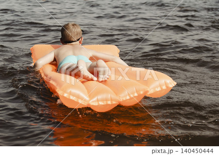 little boy joyfully plays orange inflatable mattress river, creating bright splashes around him. image conveys carefree joy and energy childhood summer day. water activities childre, family vacations little boy joyfully plays orange inflatable mattress river, creating bright splashes around him. image conveys carefree joy and energy childhood summer day. water activities childre, family vacations 140450444
