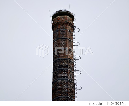 Tall brick chimney with metal ladder against cloudy sky 140450564