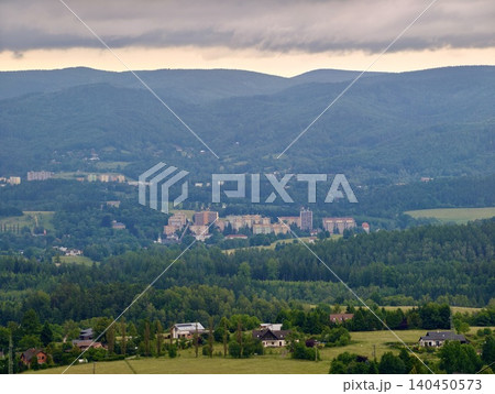 Mountain valley landscape with forested hills, village buildings, and cloudy sky Mountain valley landscape with forested hills, village buildings, and cloudy sky 140450573