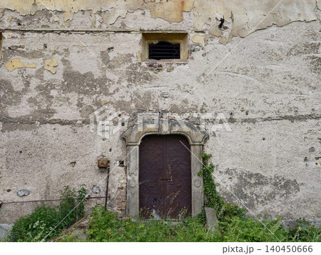 Weathered stone doorway with overgrown weeds and cracked plaster wall Weathered stone doorway with overgrown weeds and cracked plaster wall 140450666