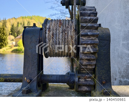 Antique Mechanical Device With Nature. Old Winch Mechanism Surrounded By Moss And Tranquil Waters Antique Mechanical Device With Nature. Old Winch Mechanism Surrounded By Moss And Tranquil Waters 140450981