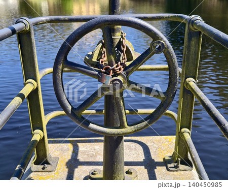 Aged Industrial Valve On Dockside Highlights Resilience Amid Tranquil Canal Setting And Weathered Surfaces Aged Industrial Valve On Dockside Highlights Resilience Amid Tranquil Canal Setting And Weathered Surfaces 140450985