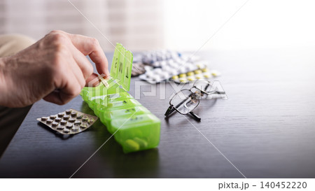 Middle aged caucasian man distributing scheduled dose of medication in dosette box 140452220