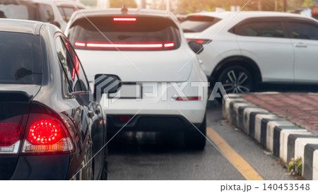 Black sedan with turn on tail light is stopped next to a modern white car during an evening traffic jam. Other commuter vehicles long queue to make a U-turn on asphalt road. Black sedan with turn on tail light is stopped next to a modern white car during an evening traffic jam. Other commuter vehicles long queue to make a U-turn on asphalt road. 140453548