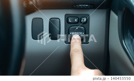 Close-up shot of a finger pressing the electric side mirror control switch button. On a car interior dashboard console panel illustrating driver adjustment adjustments. Close-up shot of a finger pressing the electric side mirror control switch button. On a car interior dashboard console panel illustrating driver adjustment adjustments. 140453550