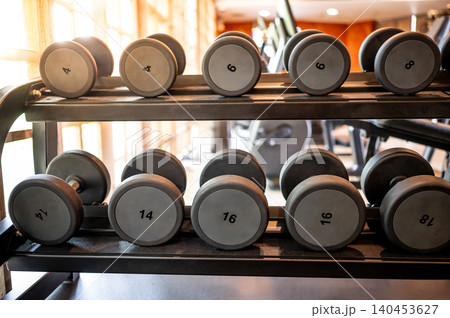 Set of dumbbells lined up by size on metal gym rack 140453627