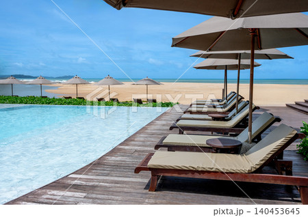 Luxury resort hotel with swimming pool and beach chairs or loungers under umbrellas Luxury resort hotel with swimming pool and beach chairs or loungers under umbrellas 140453645