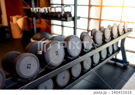Set of dumbbells lined up by size on metal gym rack 140453818