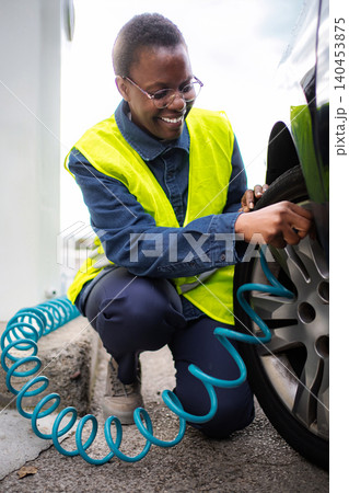 Happy woman checking inflating car tire at gas station Happy woman checking inflating car tire at gas station 140453875