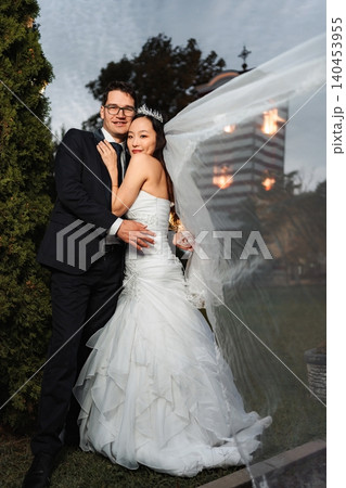 Interracial wedding couple embracing with bride's veil flowing Interracial wedding couple embracing with bride's veil flowing 140453955