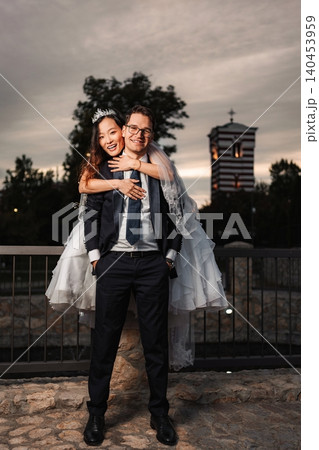 Happy interracial married couple having piggyback ride outdoors Happy interracial married couple having piggyback ride outdoors 140453959