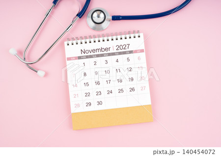November 2027 desk calendar and Medical stethoscope on pink background. November 2027 desk calendar and Medical stethoscope on pink background. 140454072