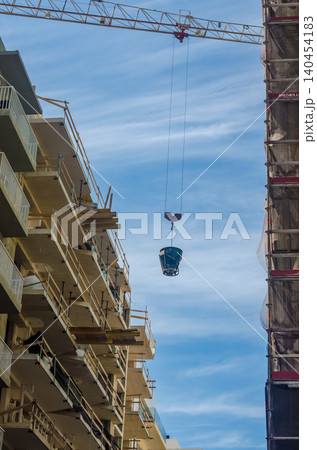 Tower Crane Lifting Concrete Bucket Between Buildings Under Construction Site Blue Sky Multi Story Development Vertical Photo Tower Crane Lifting Concrete Bucket Between Buildings Under Construction Site Blue Sky Multi Story Development Vertical Photo 140454183