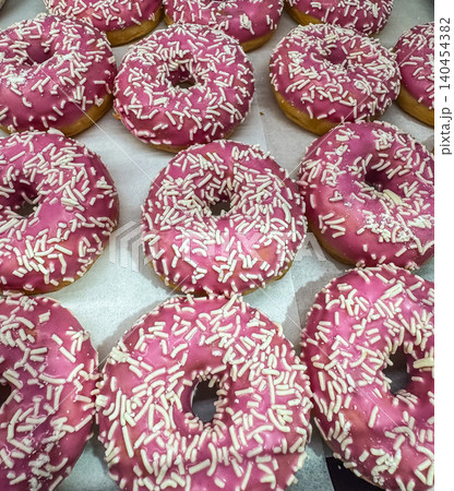 Group of fresh donuts with pink strawberry glaze and white sprinkles in a bakery. Close-up view of sweet glazed doughnuts. 140454382