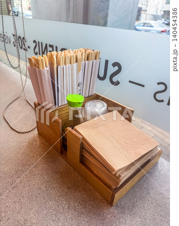 Wooden organizer with chopsticks, soy sauce bottle, napkins on restaurant counter near window. Asian dining tabletop setup. 140454386