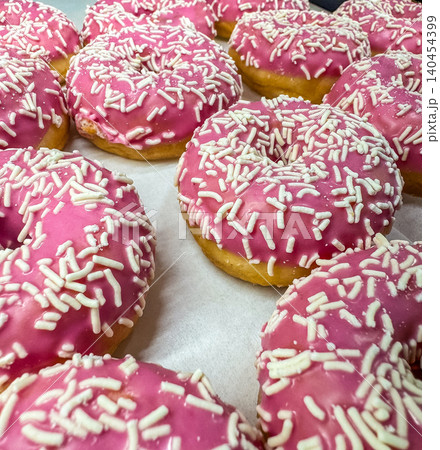 Group of fresh donuts with pink strawberry glaze and white sprinkles in a bakery. Close-up view of sweet glazed doughnuts. 140454399