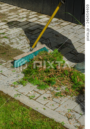 Professional Garden Maintenance: Sweeping Conifer Branch Clippings on Stone Pavement Tiles with a Turquoise Push Broom Outdoors Professional Garden Maintenance: Sweeping Conifer Branch Clippings on Stone Pavement Tiles with a Turquoise Push Broom Outdoors 140454409