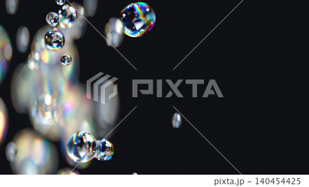 3D render of liquid spheres with iridescent effect and rainbow chromatic aberration. Defocused liquid bubbles floating in empty space on a soft black background. 140454425