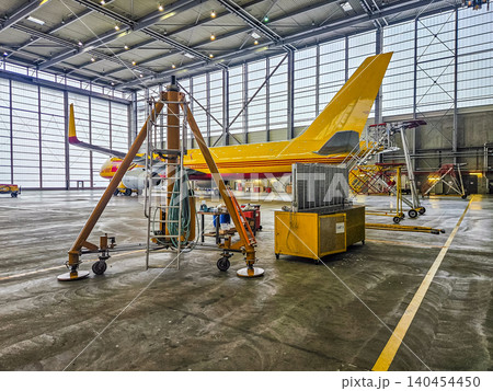 Large cargo airplane inside a maintenance hangar with technical equipment, ladders, and yellow support stands. Large cargo airplane inside a maintenance hangar with technical equipment, ladders, and yellow support stands. 140454450