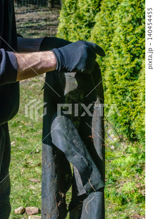 Worker in gloves holding black landscaping fabric weed barrier geotextile membrane for backyard garden maintenance and protection. Worker in gloves holding black landscaping fabric weed barrier geotextile membrane for backyard garden maintenance and protection. 140454455