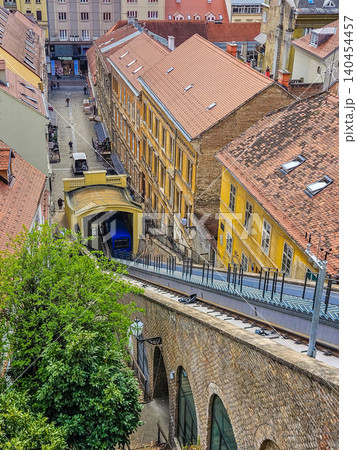 Zagreb Funicular in Croatia, blue cable car on steep tracks surrounded by historic yellow buildings and orange rooftops. Zagreb Funicular in Croatia, blue cable car on steep tracks surrounded by historic yellow buildings and orange rooftops. 140454457