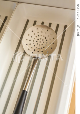 Stainless steel kitchen skimmer with a black handle against a striped white background. Essential cooking utensil. Stainless steel kitchen skimmer with a black handle against a striped white background. Essential cooking utensil. 140454490