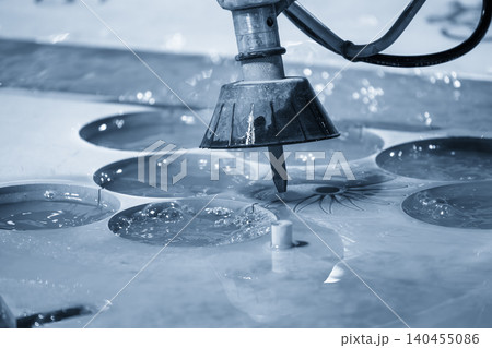 High-pressure abrasive water jet cutting machine processing a metal plate in a blue-toned industrial scene. 140455086