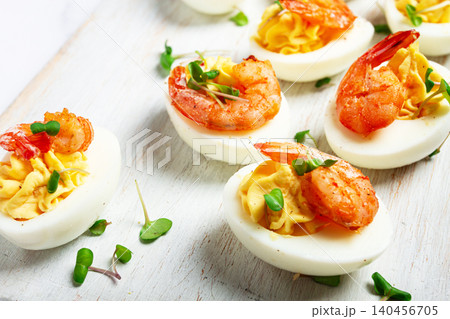 Boiled eggs stuffed with yolk and seasoned with mayonnaise, stuffed eggs with shrimp, on a white wooden chopping board, selective focus, close-up, without people, Boiled eggs stuffed with yolk and seasoned with mayonnaise, stuffed eggs with shrimp, on a white wooden chopping board, selective focus, close-up, without people, 140456705