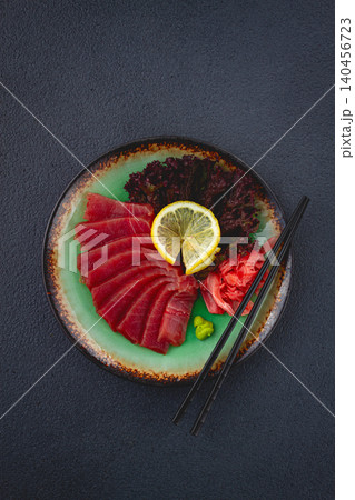 Fresh tuna sashimi served with lemon, wasabi, and pickled ginger on a dark background Fresh tuna sashimi served with lemon, wasabi, and pickled ginger on a dark background 140456723