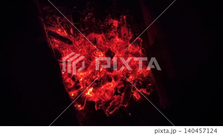 Close up of glowing charcoal embers burning with red and orange tones at night. Soft heat and shimmering texture create magical atmosphere. Warm abstract scene symbolizing warmth and quiet at nature 140457124